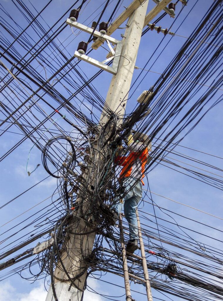 disorganized tangled wires on a telephone pole trying to be organized by a lineman