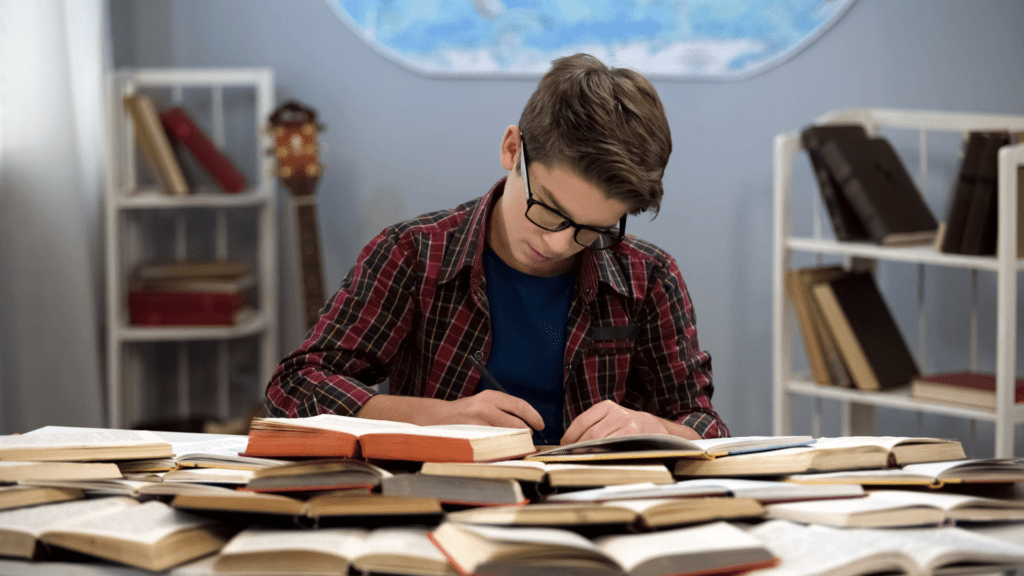 A young boy engrossed in reading a book, surrounded by a collection of books on a table.