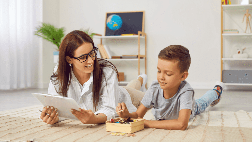 A mother and child sitting at a table, with the child playing with a toy and the mother teaching her by showing notes and explaining something.