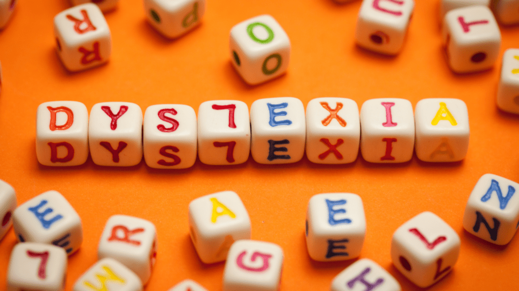 Image featuring an orange background with blocks arranged to spell 'DYSLEXIA'. Each block contains one letter, with some letters correctly oriented and others flipped or inverted, symbolizing the challenges of dyslexia.